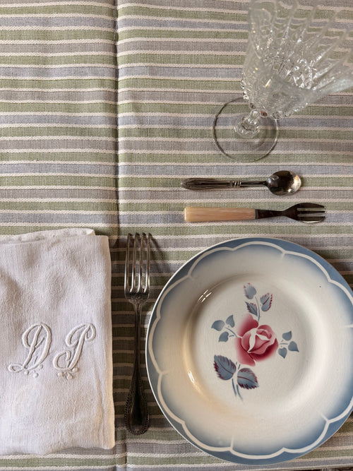 Nappe Louise à rayures vert sauge, bleu grisé, beige et écru, présentée avec une assiette ancienne fleurie et une serviette brodée – Maison Bellie.
